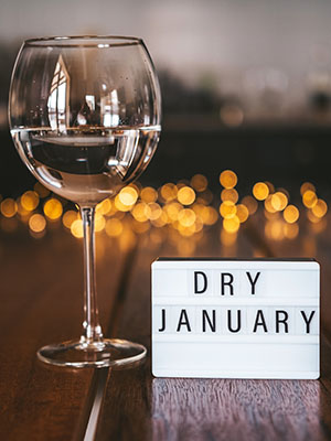 A wine glass filled with water sits next to a small marquis sign that reads Dry January