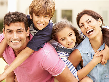 a smiling family of four with the sun shining behind them